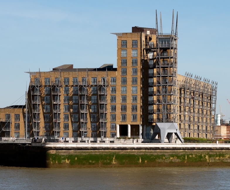 A view of a multi-story residential building located along the riverside at Putney Wharf, SW15, featuring brick walls, several balconies, and large windows. The building is situated on the bank of a r